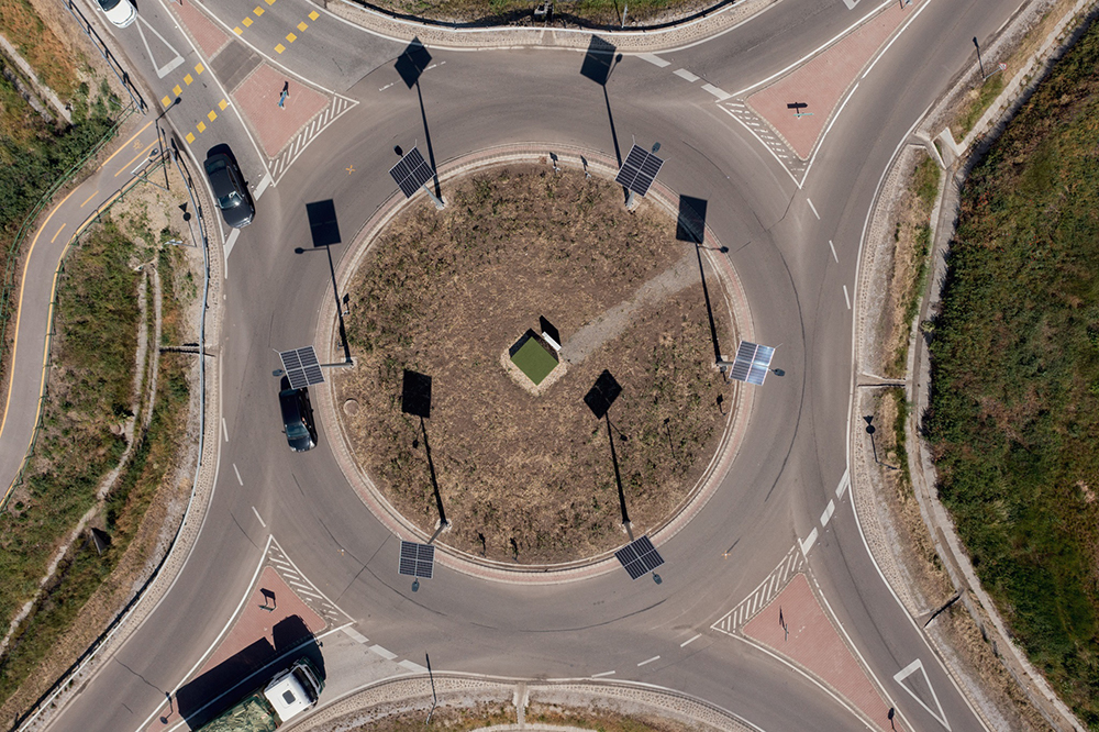 The lamp poles - which are casting long black shadows - are located only on the roundabout island and at a bicycle crossing